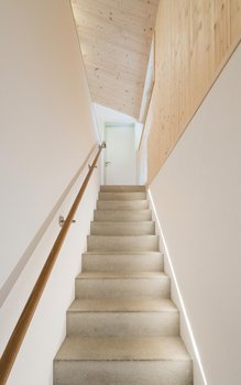 Moderne Treppe mit Betonstufen, Holzgeländer und einer Holzdeckenverkleidung, die zu einer gut beleuchteten oberen Etage führt.