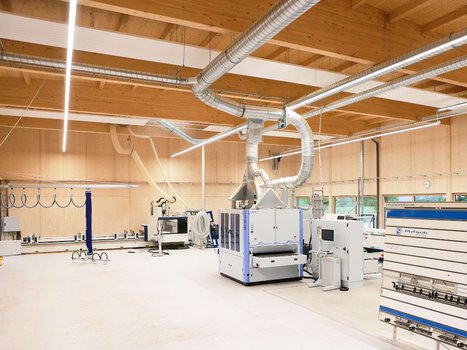 Innenaufnahme einer Werkstatt mit moderner Holzausstattung und Lüftungsrohren unter der Decke. Die ist ein Beispiel für die Rehklau Vollholz Referenzen im industriellen Bereich.