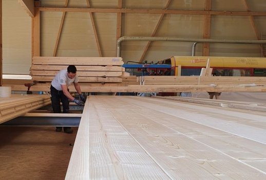 Ein Mitarbeiter arbeitet in der Rehklau-Werkstatt an einer Holzplatte. Der Raum ist von Holzbalken und Werkzeugen umgeben.