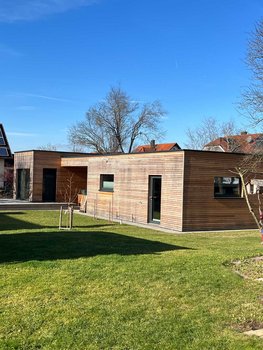 Ein modernes Gebäude von Rehklau Vollholz gebaut. Das Haus steht auf einer grünen Wiese unter einem klaren blauen Himmel und stellt eine der Referenzen für nachhaltiges Bauen dar.