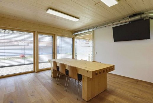 Ein moderner Konferenzraum mit Holzmöbeln von Rehklau. Große Fenster sorgen für eine helle Atmosphäre und bieten Ausblick auf das Außengelände.