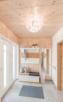 Einladender Eingangsbereich mit holzverkleideten Wänden und Decke, eleganter weißer Kronleuchter, eingebauter Sitzbank und dekorativen Spiegeln.