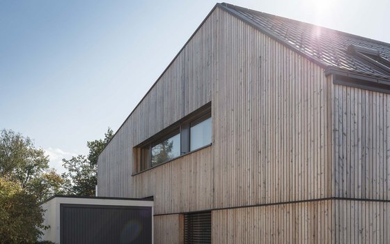 Modernes, zweistöckiges Gebäude mit holzverkleideter Fassade, großen Fenstern und einem schwarzen Dach.
