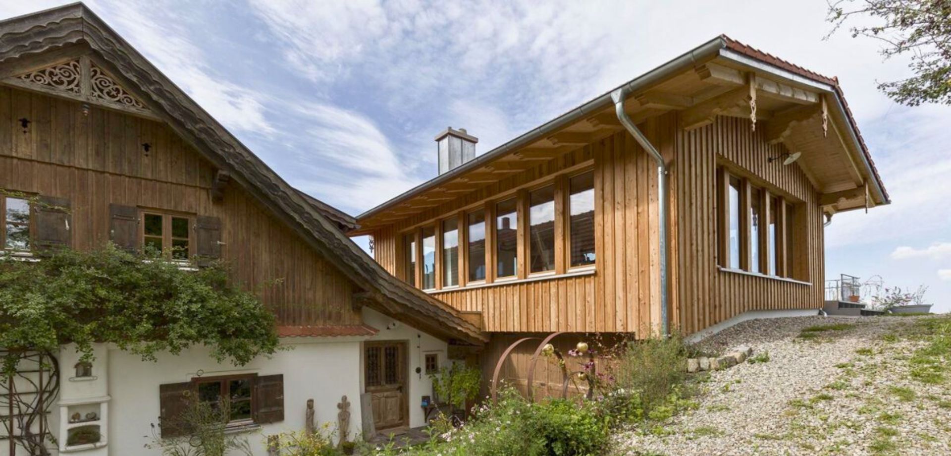 Ein Haus, das traditionelle und moderne Architektur kombiniert. Der linke Teil besteht aus dunklem Holz mit Verzierungen, während der rechte Teil eine moderne Holzverkleidung und große Fenster hat.