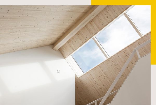 Innenansicht eines Treppenhauses mit Holzdecke und einem großen Fenster, das viel natürliches Licht hereinlässt.