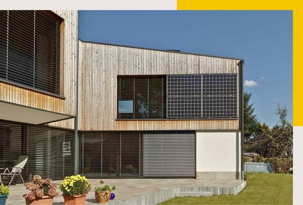 Ein Haus mit vertikalen Holzpaneelen und großen Fenstern. Es hat einen bepflanzten Außenbereich mit Blumentöpfen.