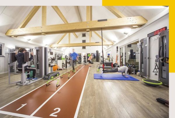 Rehklau Referenz für Zimmerei-Arbeit: Innenraum eines Fitnessstudios mit Laufbahn, verschiedenen Trainingsgeräten und Menschen, die trainieren.